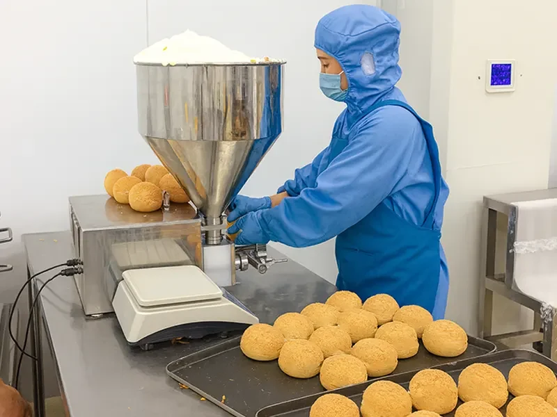 Bakery worker using automated machine to fill choux pastries with stable custard cream for automated filling and commercial baking production